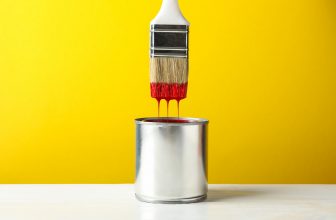 Paint can and brush against yellow background, space for text