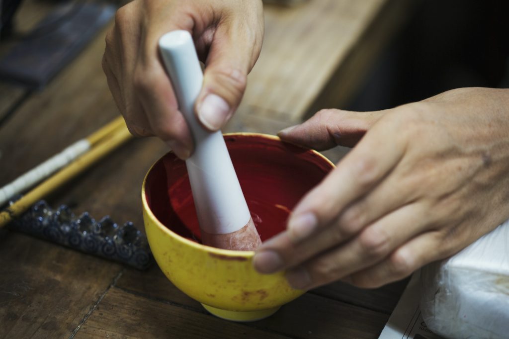 Person mixing red paint with pestle and mortar.